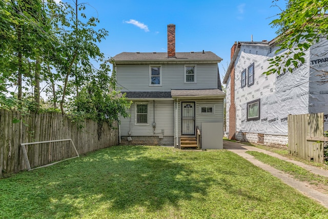 rear view of property featuring a yard, entry steps, fence, and a chimney