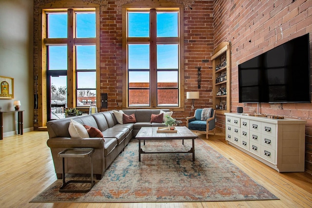 living area featuring light wood finished floors, brick wall, and a high ceiling