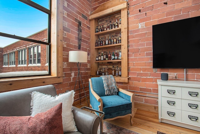 sitting room featuring brick wall, built in features, indoor wet bar, and wood finished floors