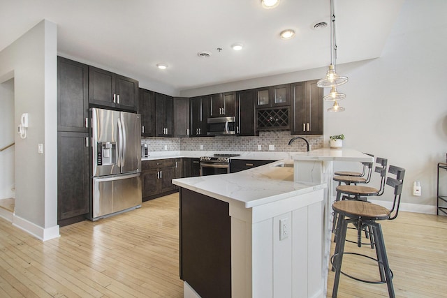 kitchen with stainless steel appliances, a peninsula, a sink, backsplash, and decorative light fixtures