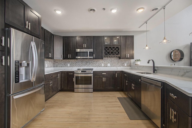 kitchen featuring light stone counters, pendant lighting, appliances with stainless steel finishes, glass insert cabinets, and a sink