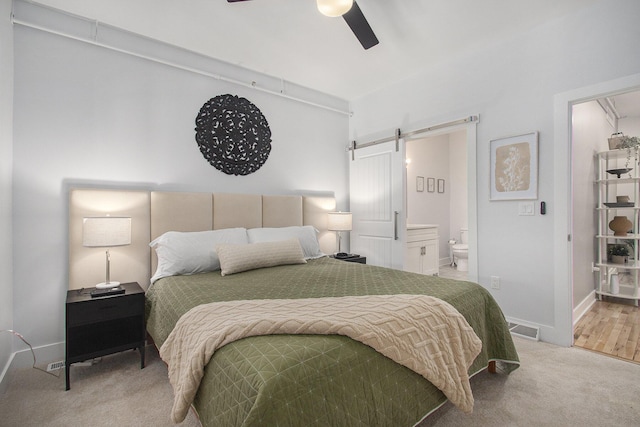 bedroom featuring carpet, visible vents, ensuite bathroom, a barn door, and baseboards