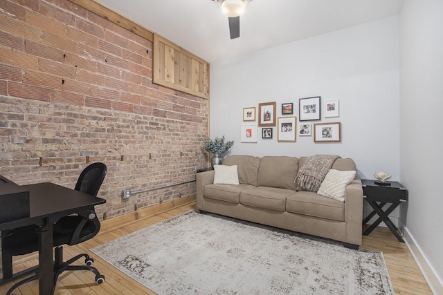 home office with brick wall, light wood-type flooring, a ceiling fan, and baseboards