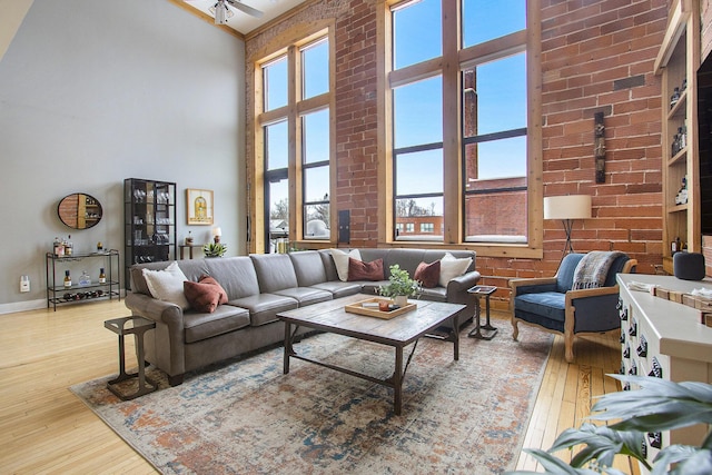 living area with light wood-style floors, a towering ceiling, and brick wall