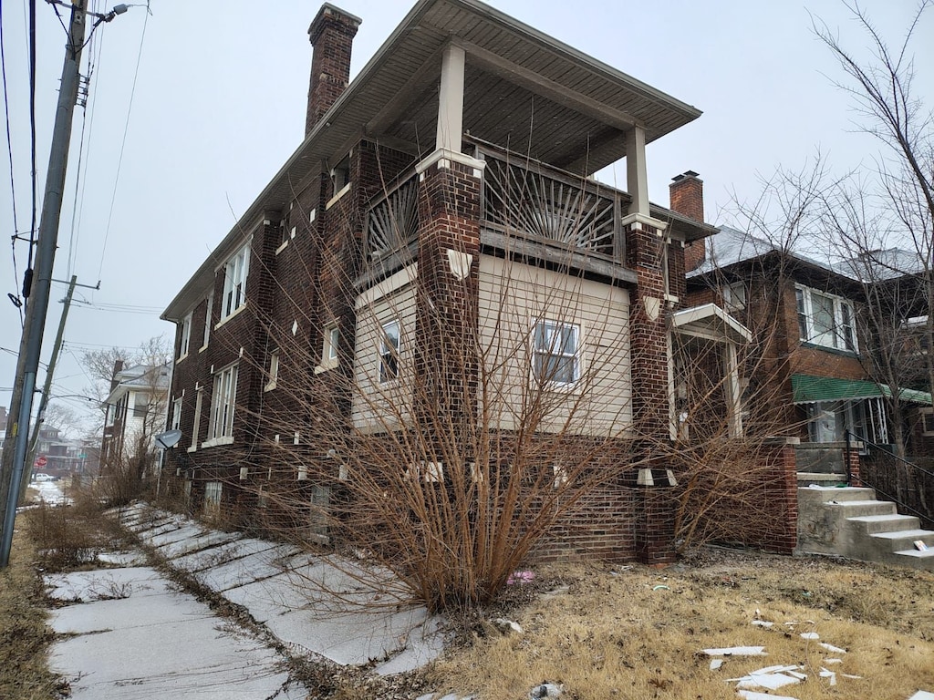 view of property exterior featuring a balcony, a chimney, and brick siding