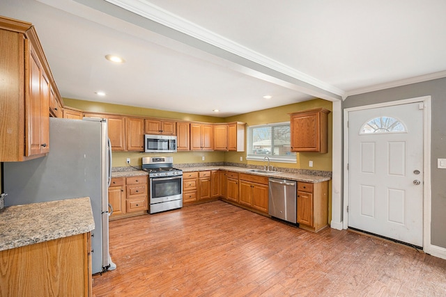 kitchen featuring light wood finished floors, stainless steel appliances, recessed lighting, ornamental molding, and a sink