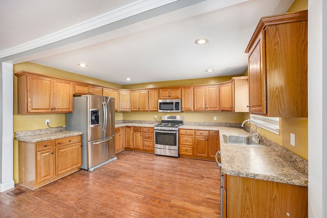 kitchen with recessed lighting, light wood-style flooring, appliances with stainless steel finishes, brown cabinetry, and a sink