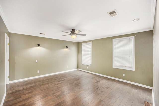 empty room with crown molding, wood finished floors, visible vents, and baseboards