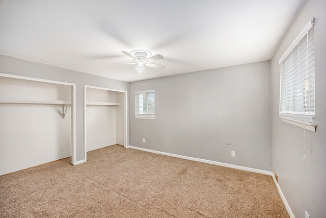 unfurnished bedroom with carpet flooring, ceiling fan, baseboards, and two closets