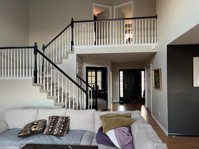 living area featuring a high ceiling, stairway, baseboards, and wood finished floors