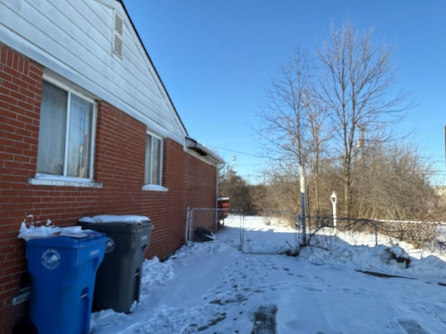 view of snowy exterior featuring brick siding and fence