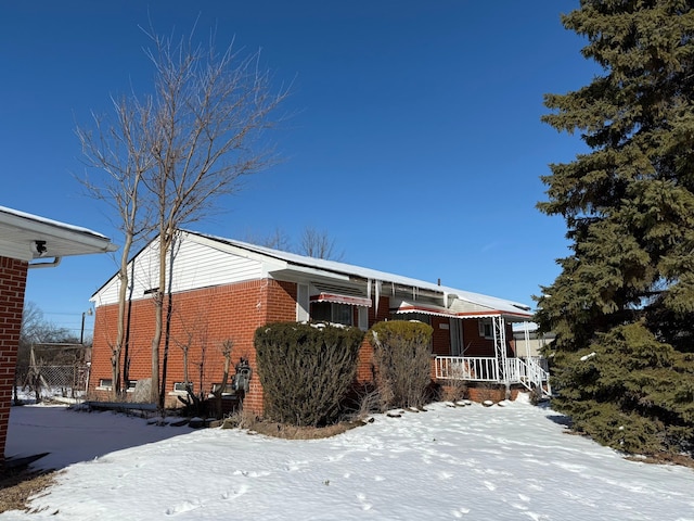 view of snow covered exterior with a porch and brick siding