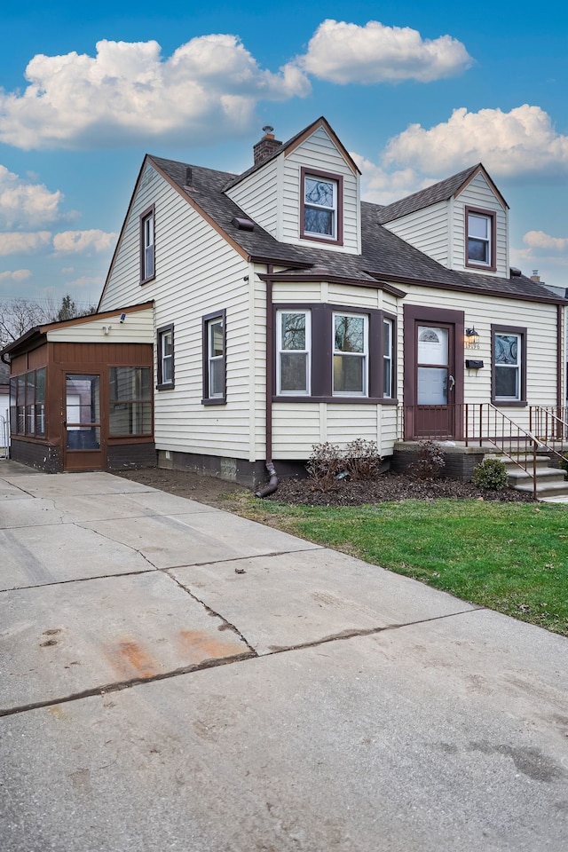 view of front of house with a shingled roof, a front yard, and a chimney