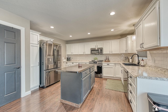 kitchen with appliances with stainless steel finishes, white cabinets, a kitchen island, a sink, and wood finished floors