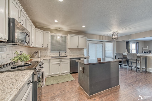 kitchen with hanging light fixtures, white cabinetry, appliances with stainless steel finishes, and a sink