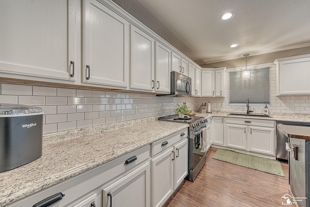 kitchen featuring pendant lighting, appliances with stainless steel finishes, light wood-style floors, white cabinetry, and a sink