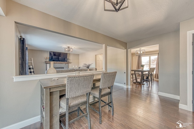 dining room featuring a textured ceiling, baseboards, a chandelier, and wood finished floors