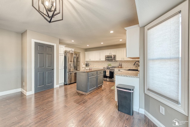 kitchen with decorative light fixtures, stainless steel appliances, white cabinets, a kitchen island, and a sink