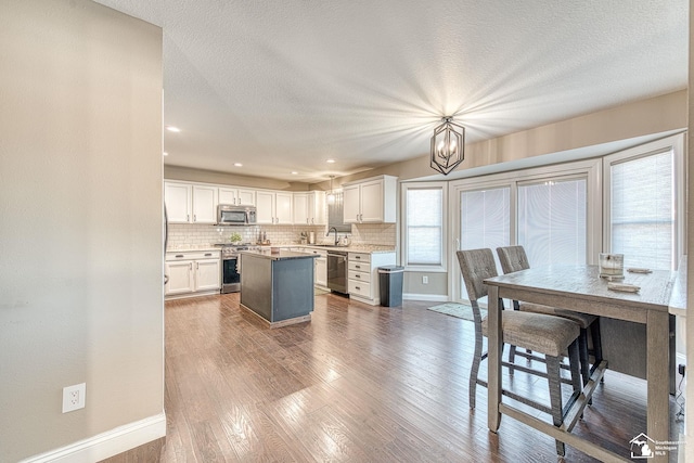 kitchen with stainless steel appliances, a kitchen island, white cabinets, hanging light fixtures, and light countertops