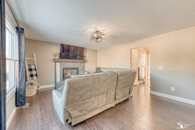 bedroom with visible vents, baseboards, a glass covered fireplace, wood finished floors, and a textured ceiling