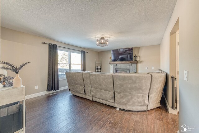 living area with a textured ceiling, a fireplace, wood finished floors, visible vents, and baseboards