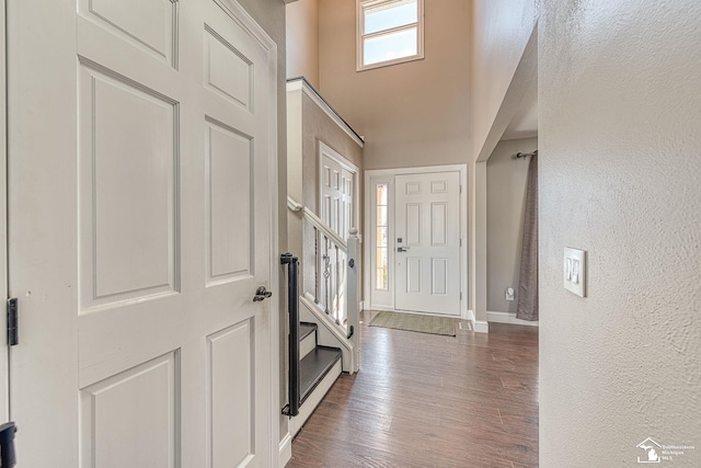 entrance foyer featuring dark wood finished floors, a textured wall, a towering ceiling, baseboards, and stairs