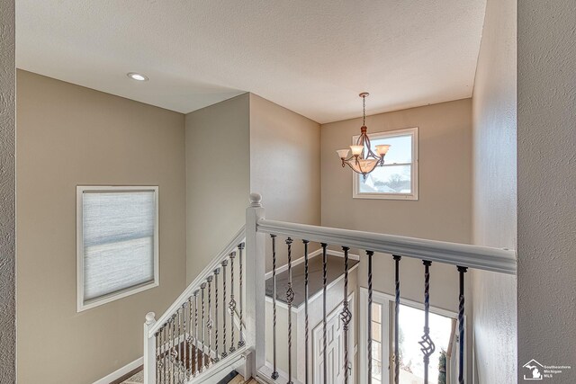 staircase with a textured ceiling, baseboards, and an inviting chandelier