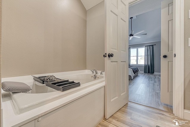 ensuite bathroom featuring a ceiling fan, connected bathroom, wood finished floors, a garden tub, and a textured ceiling