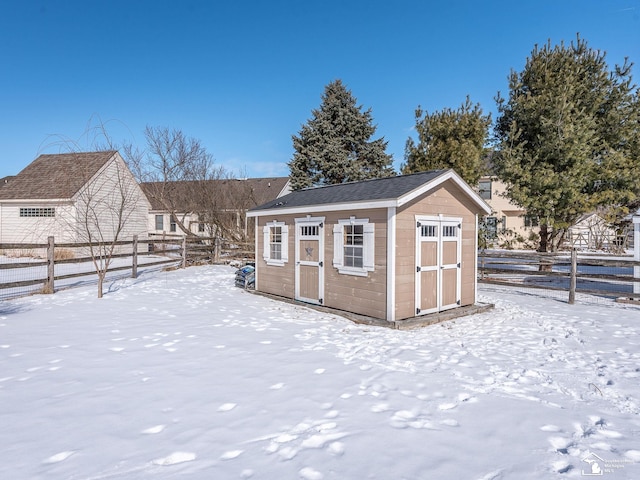 snow covered structure featuring an outbuilding, a shed, and fence