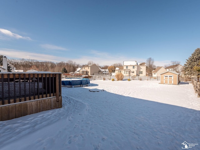 yard layered in snow with an outbuilding, fence, a residential view, a fenced in pool, and a shed