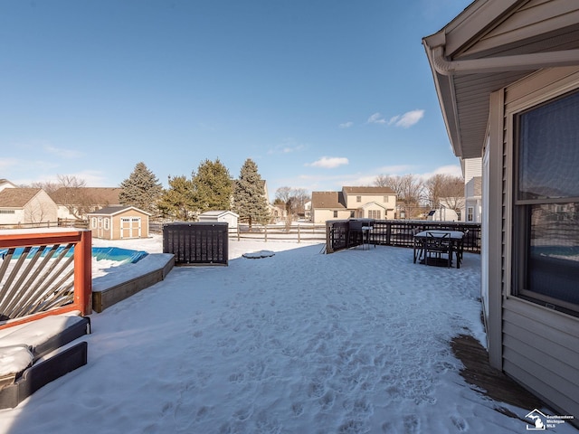 yard layered in snow with outdoor dining area, a storage unit, fence, a residential view, and an outdoor structure