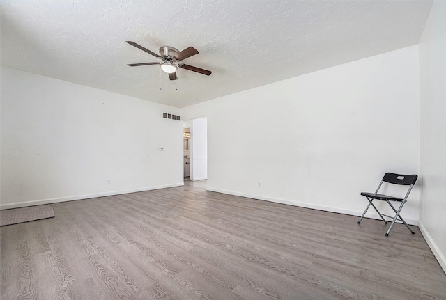 empty room with ceiling fan, a textured ceiling, visible vents, baseboards, and light wood-style floors