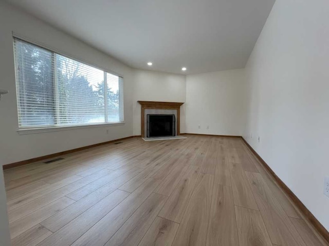 unfurnished living room featuring light wood-style flooring, visible vents, baseboards, and a fireplace with flush hearth