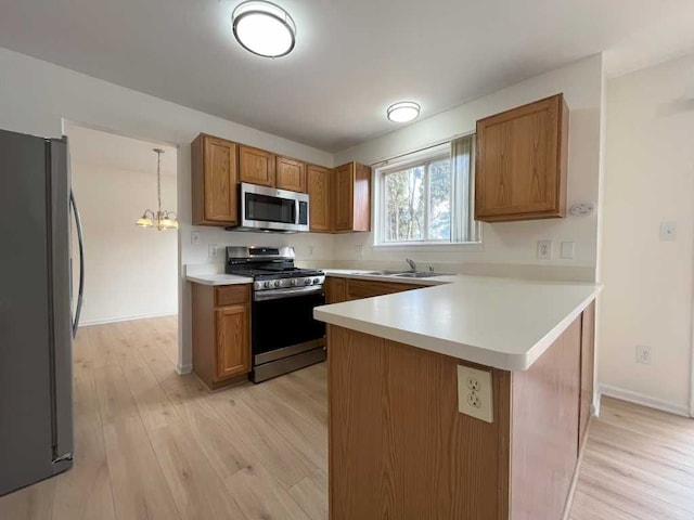 kitchen with brown cabinetry, appliances with stainless steel finishes, hanging light fixtures, a peninsula, and light countertops