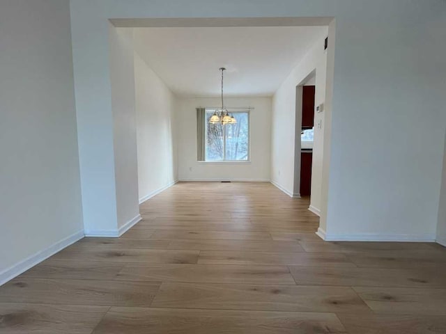 unfurnished dining area with baseboards, light wood-style floors, and a notable chandelier