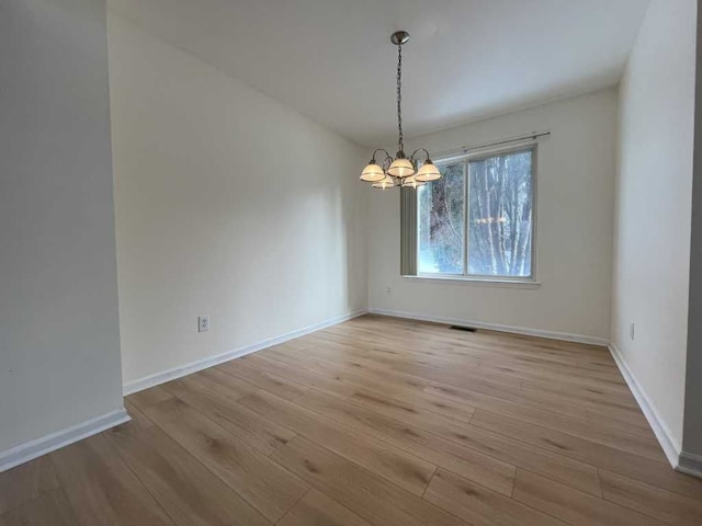 spare room with light wood-type flooring, visible vents, baseboards, and a notable chandelier