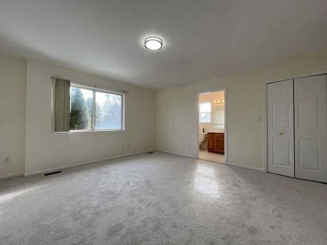 unfurnished bedroom featuring light colored carpet, visible vents, baseboards, and ensuite bathroom