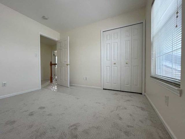 unfurnished bedroom with baseboards, a closet, and light colored carpet