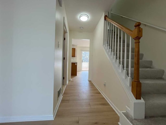 hallway with visible vents, stairs, light wood-style flooring, and baseboards