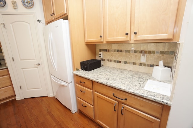 kitchen featuring freestanding refrigerator, decorative backsplash, wood finished floors, and light stone countertops