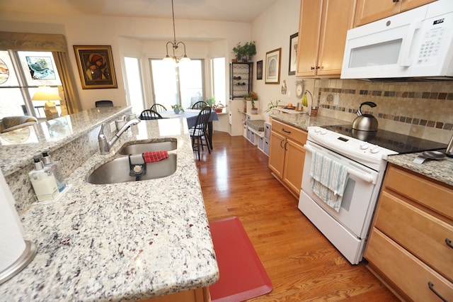 kitchen featuring white appliances, a sink, light wood-type flooring, tasteful backsplash, and decorative light fixtures