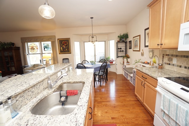 kitchen with white appliances, decorative light fixtures, a sink, and light wood-style floors