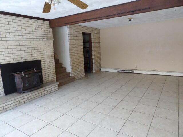 unfurnished living room featuring light tile patterned floors, ceiling fan, beamed ceiling, and a wood stove