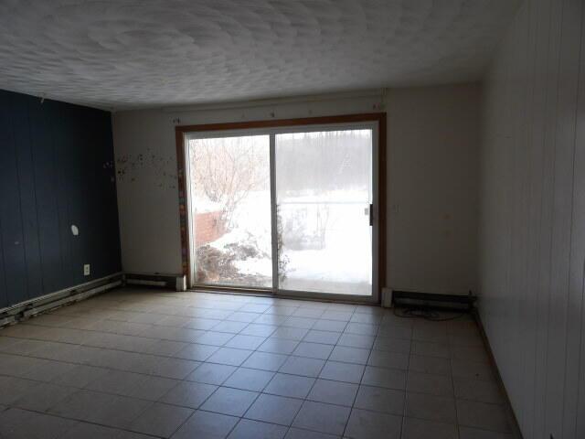 empty room featuring a textured ceiling, light tile patterned floors, and wooden walls