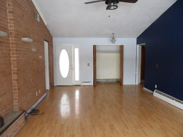 entrance foyer featuring light wood-type flooring, a baseboard radiator, visible vents, and vaulted ceiling