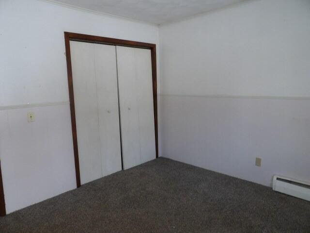 unfurnished bedroom with carpet floors, a closet, and baseboard heating