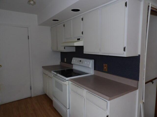 kitchen featuring under cabinet range hood, white electric stove, white cabinets, and dark wood finished floors