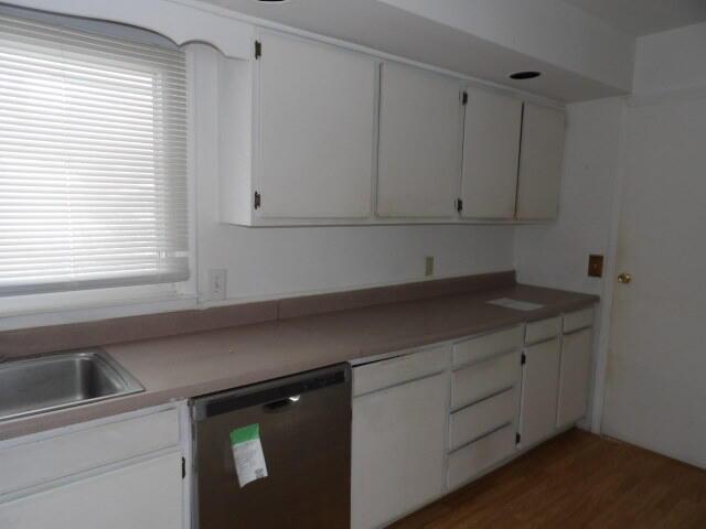 kitchen with light countertops, dark wood-style flooring, white cabinets, and dishwasher