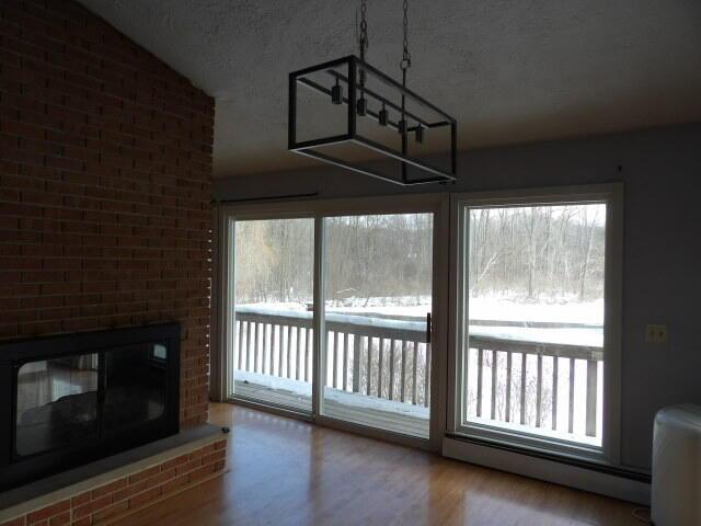 interior space featuring a fireplace, lofted ceiling, a baseboard heating unit, a textured ceiling, and wood finished floors