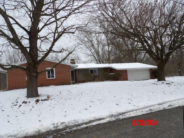 single story home featuring a garage, a chimney, and brick siding